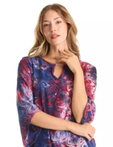 Blusa Ruby Rd. de corte holgado con diseño texturizado y estampado floral en tonos azul y bordó. Presenta cuello redondo con escote tipo keyhole y detalle metálico, mangas tres cuartos amplias y dobladillo asimétrico.