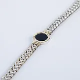Pulsera de cadena tejida en plata con detalle central circular en oro que enmarca una piedra ónix negra.