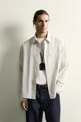 Camisa relaxed fit de algodón con estructura, cuello solapa, manga larga con puño abotonado, bolsillo de parche en el pecho y cierre frontal con botones. Presenta diseño de rayas finas.