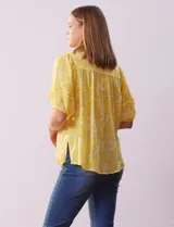 Blusa amarilla estampada con cuello en V, manga corta con volados y ruedo anudado.