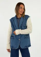 Campera híbrida con cuerpo de denim azul y mangas tejidas de lana en color crema con diseño de ochos. Presenta solapas, cierre frontal con botón, bolsillos delanteros con solapa y bordes deshilachados en las sisas.