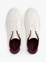 Zapatillas de cuero estilo tenis, color blanco, con cordones y suela de goma al tono. Presentan forro interior en color bordó, ojal superior metálico dorado y logo de monograma TH metálico en el lateral.