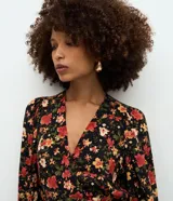 Enterito corto de viscosa con estampado floral sobre fondo negro, escote en V, mangas largas con volumen y puños ajustados.