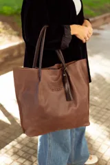 Bolso tote de cuero color marrón con asas de cuero negro y detalle de borla de cuero negro.