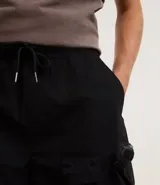 Bermuda masculina de poliéster color negro, corte baggy cropped, con cintura elástica ajustable con cordón y bolsillos funcionales.