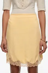 Falda mini de corte recto color blanco, con detalle de encaje en el bajo y cintura elástica.