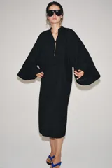 Vestido túnica largo negro de corte midi con mezcla de viscosa y lino, escote en V y mangas largas evasé. Presenta cierre frontal con alamares decorativos.