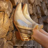 Botas cortas de cuero Carolina De Cunto, con diseño artesanal pintado a mano, combinación de texturas en tonos dorado, crema y detalles estampados, taco bloque de madera y punta fina con estilo texano.