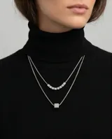 Collar doble de acero con cadenas finas. La cadena superior presenta varios cubos pequeños alineados, mientras que la cadena inferior cuenta con un dije central en forma de cubo.