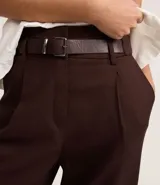 Pantalón de vestir marrón chocolate, de corte recto, con cintura alta, trabillas para cinturón, cierre con botón y cremallera, pliegues frontales y cinturón con hebilla.
