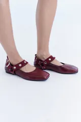 Ballerinas de cuero bordó con puntera cuadrada, diseño destalonado y tira en el empeine decorada con tachas metálicas.