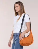 Cartera bandolera de lona naranja en forma de medialuna, con correa ajustable negra y cierre principal.