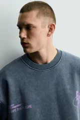 Sudadera de corte boxy fit con efecto lavado, cuello redondo y manga larga. Presenta estampados a contraste en color violeta en la parte frontal y acabados en rib en cuello, puños y ruedo.