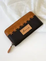Billetera grande de cuero color negro y camel, con cierre metálico y detalle de costuras cruzadas en la parte superior. Incluye monedero interno.