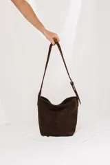 Cartera tipo morral y bandolera de gamuza marrón, con correa larga ajustable y diseño estilo hobo.