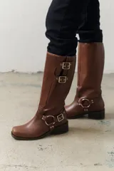 Bota de cuero negra de caña alta con herrajes plateados, hebillas y arnés.