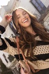 Buzo de punto calado a rayas horizontales en tonos beige y negro, con capucha y corte holgado.