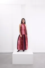 Vestido largo de corte holgado con estampado degradé en tonos rojizos y bordó. Presenta escote halter con cuello alto, espalda descubierta con cierre de botones y un maxi volado en la cadera que aporta volumen a la falda.