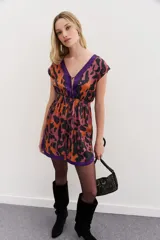 Vestido corto con escote en V y espalda semidescubierta. Presenta un estampado abstracto en tonos naranja, negro y violeta, con bordes a contratono en color violeta en el escote y el ruedo. Cuenta con cintura elástica y frunces en los hombros.