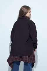 Sobrecamisa de pana color marrón oscuro, con diseño de corte amplio, cuello camisero, cierre frontal con botones y bolsillos con solapa en el pecho.
