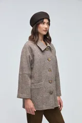 Chaquetón de lana fina sin teñir, con cuello camisero, cierre frontal de botones y bolsillos delanteros. Diseño de corte recto y estructura clásica.
