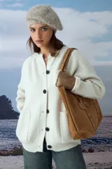 Cardigan tejido de punto en color natural, con cuello redondo, cierre frontal de botones oscuros y dos bolsillos delanteros. Presenta mangas largas con puños acanalados.