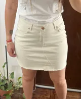 Minifalda de denim color crudo, con diseño de cinco bolsillos, cierre frontal con botón y bragueta, y ruedo desmechado.
