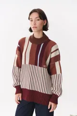 Buzo oversize de tejido de punto con diseño de bloques y rayas verticales en colores rojo, verde, bordó y crema. Presenta cuello alto tejido y terminaciones en rib en puños y ruedo.