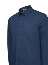 Camisa de hombre color azul marino, de manga larga con presillas para enrollar, cuello clásico, cierre de botones de madera y bolsillo en el pecho con logo bordado. Confeccionada en popelina 100% algodón orgánico.