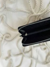 Billetera grande de cuero con cierre metálico perimetral. Presenta un diseño combinado con una sección superior de cuero liso brillante y una sección inferior de cuero con textura de reptil. Incluye el logo de la marca grabado en la parte frontal.