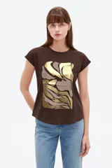 Remera de algodón color marrón, con diseño holgado, mangas cortas con vuelto y estampado frontal abstracto con detalles metalizados en tono dorado y marrón.