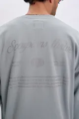 Buzo deportivo oversize verde pastel con cuello redondo, mangas largas y estampa tipográfica en la espalda.
