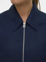 Chaqueta corta azul marino con cuello solapa, cierre frontal con cremallera y mangas largas con presilla y botón en los puños.