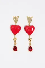 Caravanas colgantes de metal dorado con diseño de flecha decorada con cristales brillantes, un corazón rojo esmaltado y un dije inferior en forma de lágrima con cristal rojo.