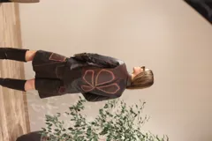 Camisa de cuero con diseño de patchwork en tonos negro y marrón oscuro, con efecto desgastado en las costuras. Presenta cuello camisero, botones frontales y mangas largas.