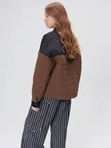 Campera capitonada de gabardina de algodón en combinación de colores marrón y negro, con cuello camisero, puños y canesú de pana negra. Cuenta con bolsillos laterales, cierre frontal oculto bajo cartera con botones a presión y relleno de guata.