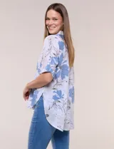 Camisa de lino sintético con estampado floral en tonos azules y beige sobre fondo blanco, de corte holgado, mangas tres cuartos y cuello camisero.