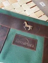 Sobre tipo cartuchera de lona naranja con detalles y apliques en cuero marrón. Presenta un aplique metálico en forma de caballo y un parche con el logo de la marca grabado en el frente.