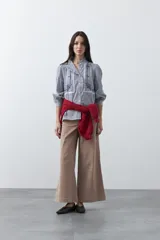 Camisa de rayas verticales con cuello mao, detalle de volados en el escote, bordados florales y recortes con calados. Posee mangas largas abullonadas con puños ajustados y cierre frontal con botones.