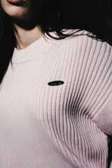 Sweater de tejido acanalado en color rosa, con cuello redondo y manga larga. Presenta un pequeño detalle bordado en el pecho.