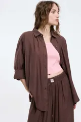 Camisa color marrón de corte oversized, con abotonadura frontal y en las mangas. Presenta un corte vertical en la espalda con lazos decorativos.