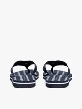 Ojotas de mujer color azul marino con tiras trenzadas de tela y una pequeña insignia metálica con el monograma TH en contraste sobre la tira del dedo. La plantilla presenta un patrón de eslabones blancos y finas líneas blancas.