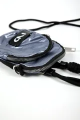 Cartera bandolera pequeña color dorado metálico, con cierre principal y bolsillo frontal con cierre. Tiene una correa ajustable de cordón negro y un parche rectangular negro con el logo "IND" en blanco.