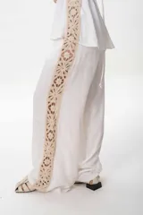 Pantalón sastrero de lino color negro con una guarda lateral de broderie color crudo que recorre el lateral desde la cintura hasta el bajo. El pantalón es de corte ancho y fluido.