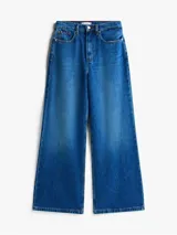 Jean de Tommy Hilfiger confeccionado en denim rígido, con corte de pierna ancha y talle alto. Presenta un diseño clásico de cinco bolsillos, cierre de cremallera con botón y un sutil efecto desteñido en muslos y rodillas.