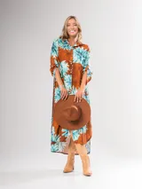 Vestido camisero largo con estampado floral en tonos rojos y negros, con cuello camisero, abotonadura frontal y mangas largas con puños abotonados.