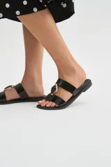 Sandalias planas color crudo con doble tira y detalle de piedra decorativa al centro con borde dorado.