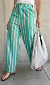Pantalón de lino a rayas verticales en tonos verde, celeste y blanco, de corte holgado, con cierre y botón, y dos bolsillos laterales.