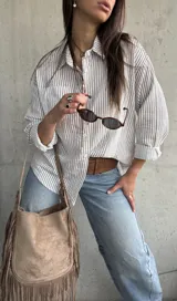 Camisa de corte oversize, con diseño a rayas verticales marrón sobre fondo blanco, manga larga, cuello camisero y bolsillos frontales.