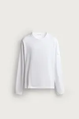 Camiseta de manga larga con cuello redondo y corte relajado. Presenta un pequeño bolsillo tipo plastrón con solapa en la manga izquierda.
